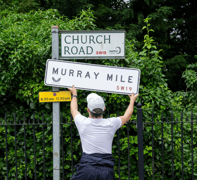 A man replaces a road sign with an Andy Murray Castore sign called Murray Mile